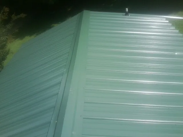 New green metal panels meeting at the ridge of a roof — Flat Roof Repair work by our crew in Statesboro