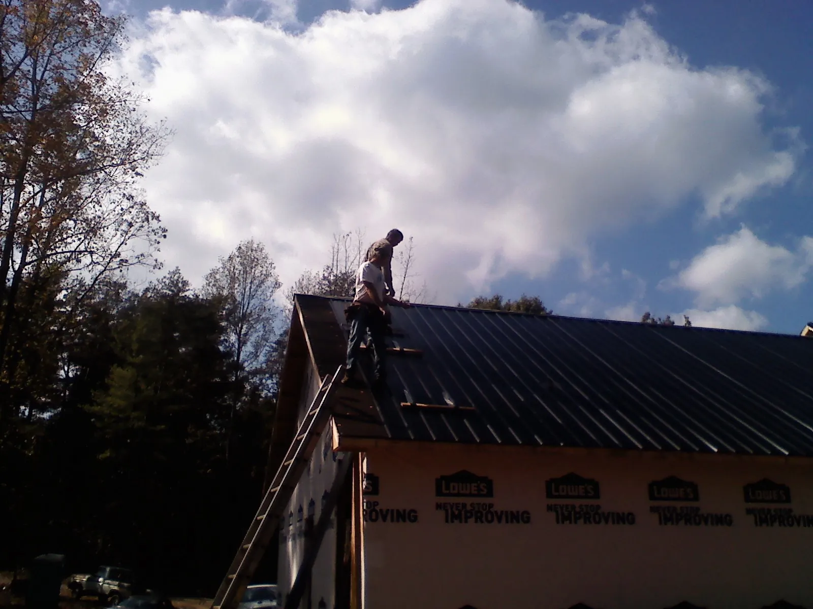 Roofer fastening dark metal panels high against a cloudy sky, from a Roof Inspection job in Statesboro