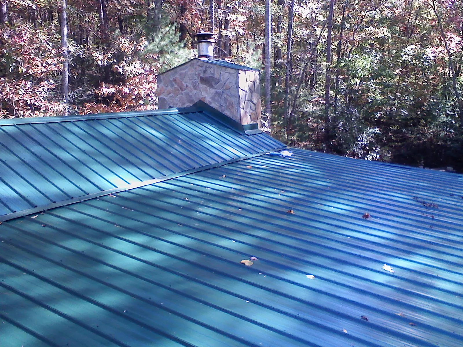 New green metal roof and stone chimney surrounded by autumn woods in Statesboro